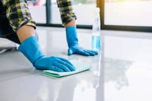 Commercial cleaner in Michigan using cleaning solution and blue gloves to wipe white tiled floors